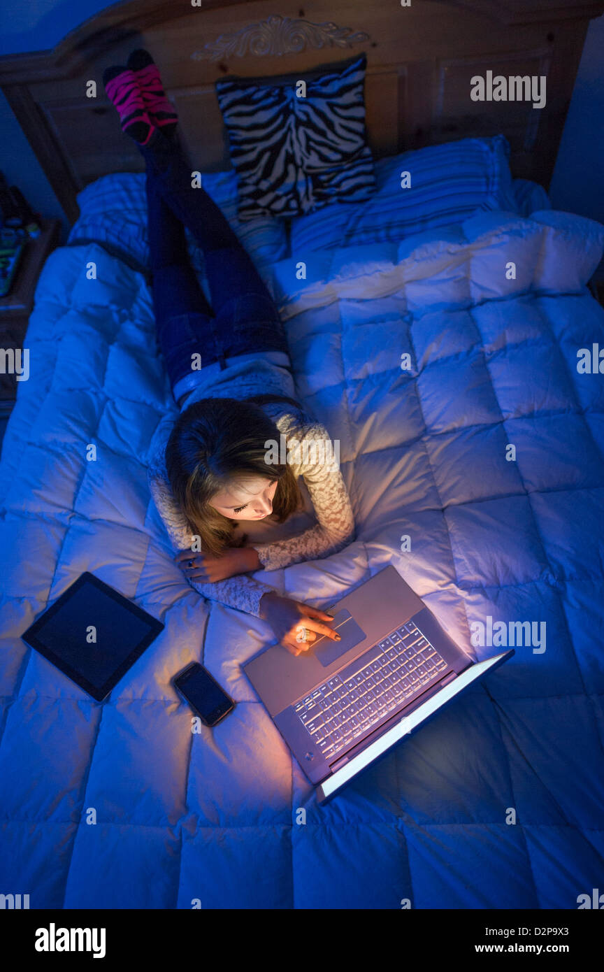 Schönes junges Mädchen lag auf einem Bett in der Nacht arbeiten auf einem Laptop. Stockfoto