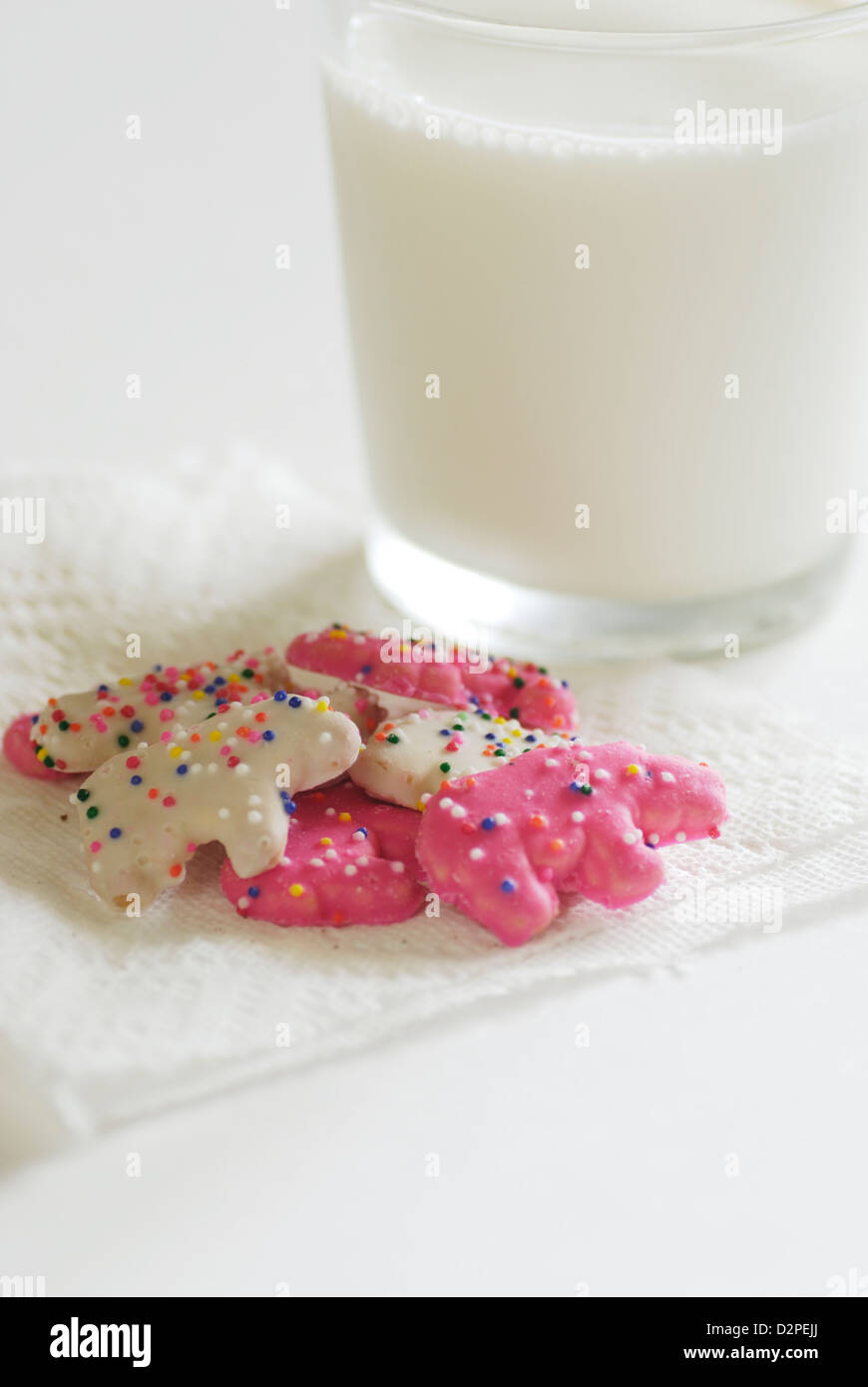 Rosa und weiß gefrostet Tier Cookies mit Streusel auf eine weiße Serviette mit einem Glas Kuhmilch Stockfoto