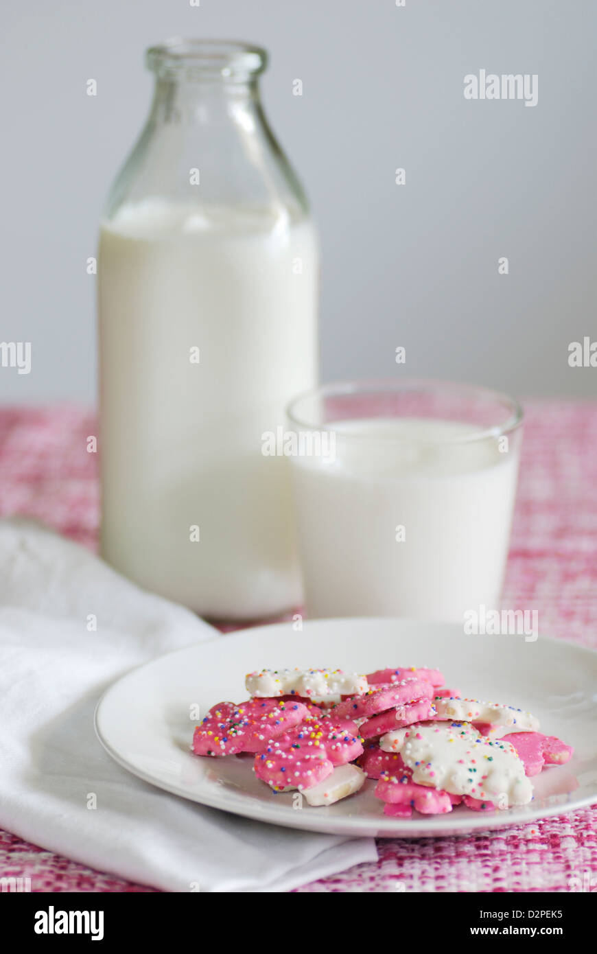 Rosa und weiß gefrostet Tier Cookies mit Streusel auf einem rosafarbenen und weißen Tweedstoff mit Flasche und Glas Kuhmilch Stockfoto