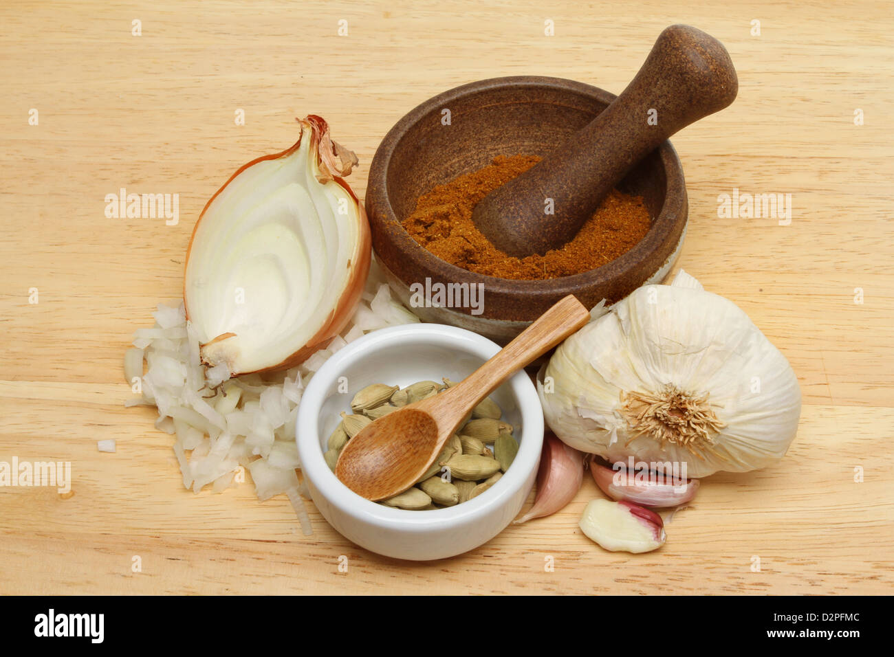 Curry-Zutaten, Zwiebel, Knoblauch, Kardamom und Curry-Pulver in einem Stößel und Mörser auf einem Holzbrett Stockfoto