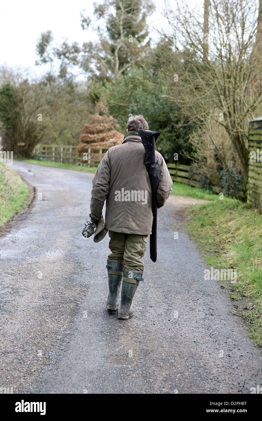 Mann zu Fuß in grün Wellie Stiefel (Gummistiefel) und Jagd Kleidung, hält er eine Schrotflinte und Gehörschutz in einem Lederetui. Stockfoto