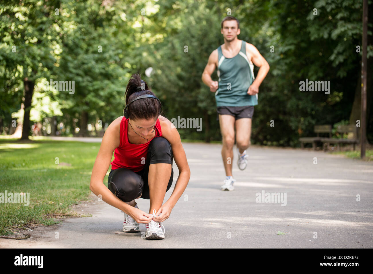 Junge Frau binden Schnürsenkel, Mann im sport hinter Joggen Stockfoto
