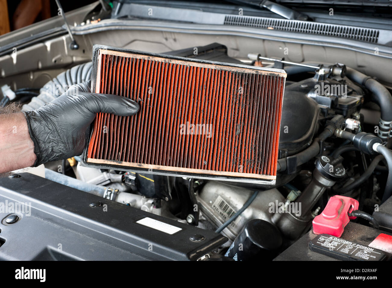 Kfz-Mechaniker tragen schützende Arbeitshandschuhe hält einen schmutzigen, verstopfte Luftfilter Stockfoto