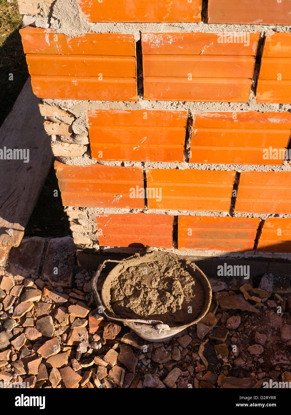 Detail einer Keramikblock Wand und den Mörtel zwischen den Blöcken zusammen mit einem Eimer Mörtel. Stockfoto