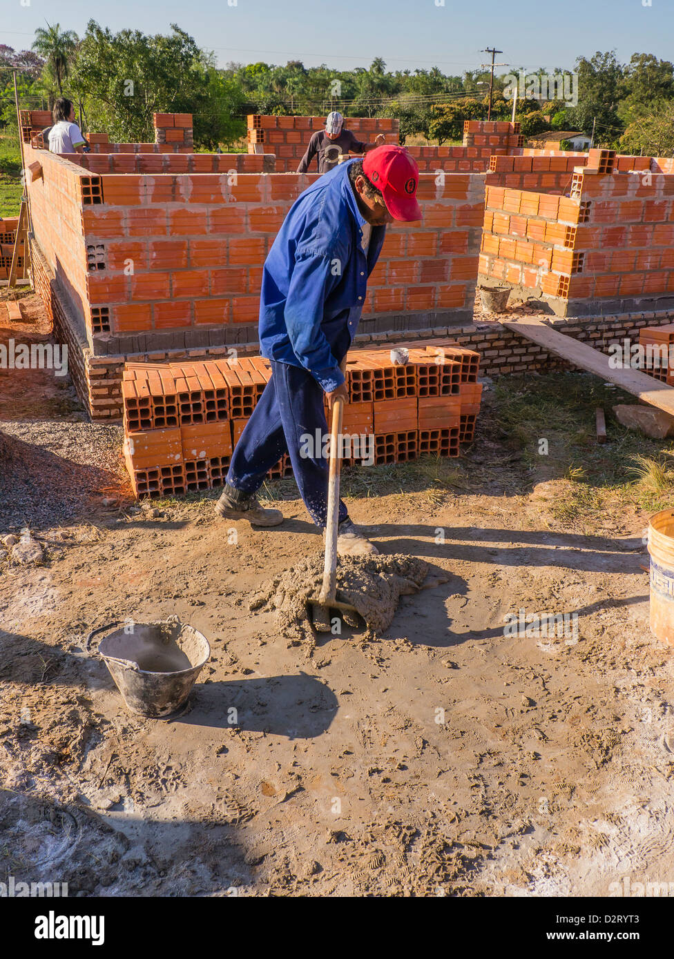 Ein spanischer Arbeitnehmer mischt Mörtel auf dem Boden für den Bau eines Hauses gebaut mit Hilfe von internationalen Freiwilligen labo Stockfoto