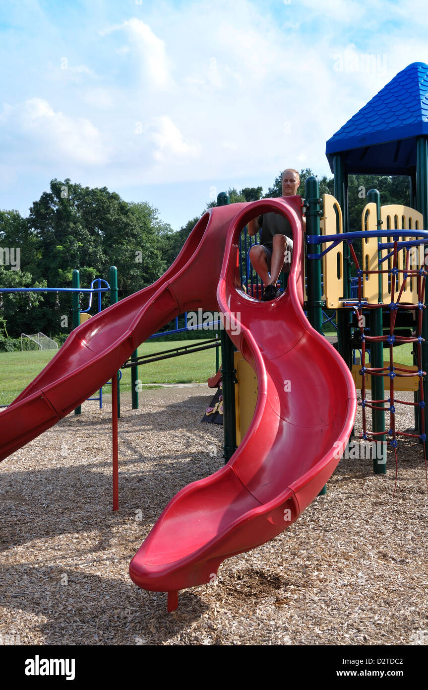 Erwachsener Mann versucht, eine Rutsche in einen Kinderspielplatz zu gehen,  als ob er seine Kindheit erinnert Stockfotografie - Alamy