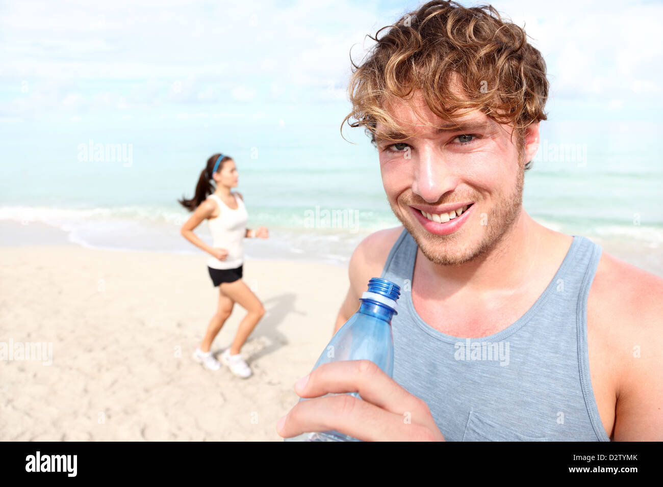 Porträt von Trinkwasser Fit junger Mann mit Frau im Hintergrund am Strand joggen Stockfoto