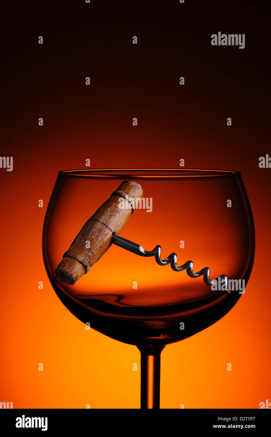 Eine antike Korkenzieher in ein Glas Wein gegen ein warmes Licht auf dunklem Hintergrund. Stockfoto