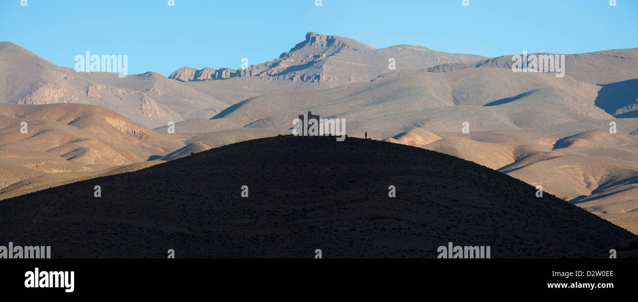 Panorama von entfernten Turm und einsamer Mann auf glatten Hügel Silhouette gegen eine bergige Wüste zurückfallen Marokko Stockfoto