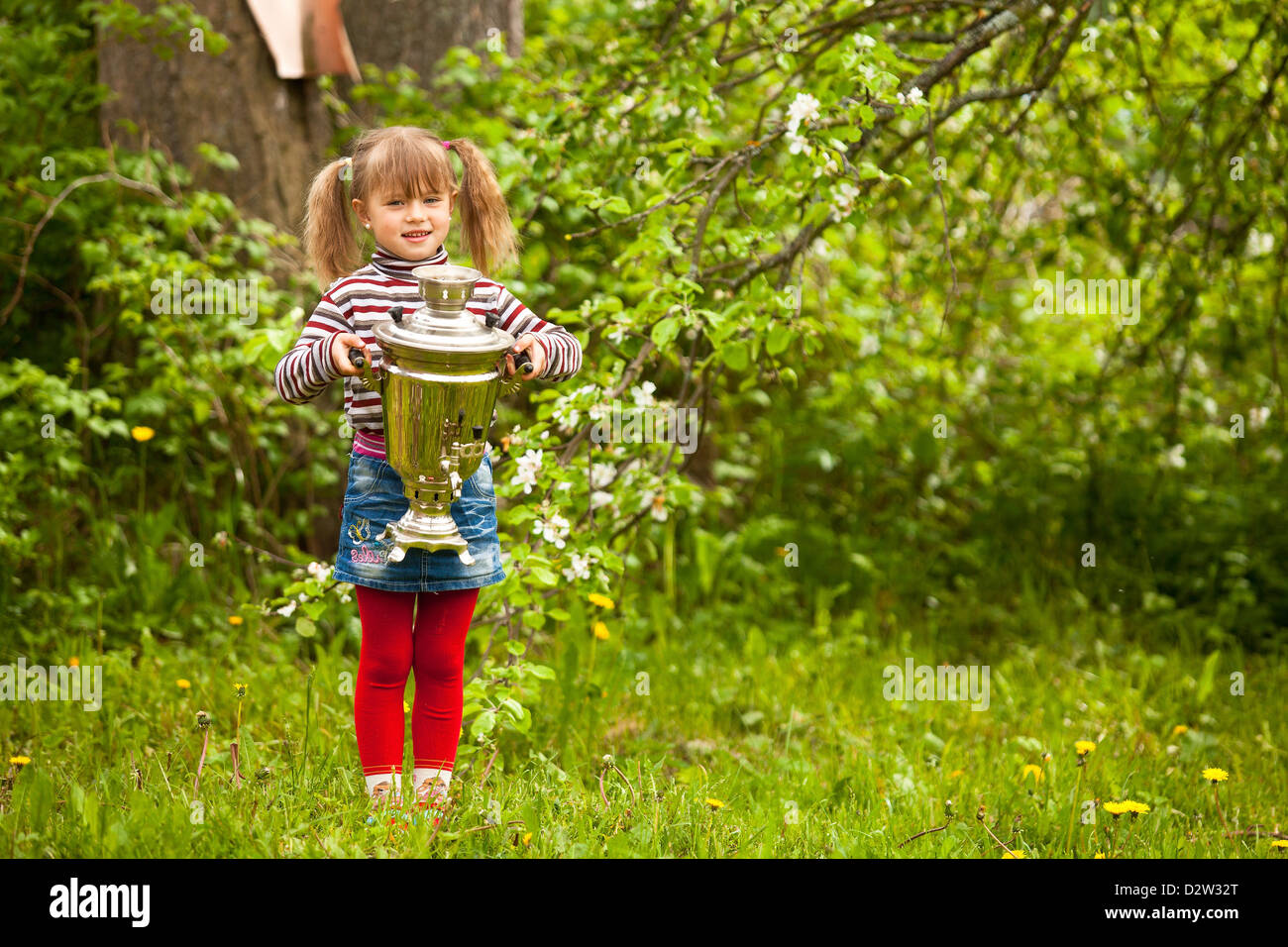 Schönes kleines Mädchen posiert mit dem russischen Samowar am Park. Stockfoto