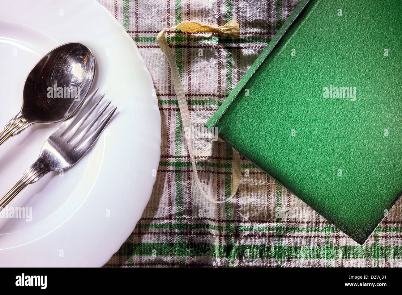 Altes grünes Buch und weißen Teller mit Gabel und Löffel drin. Stockfoto