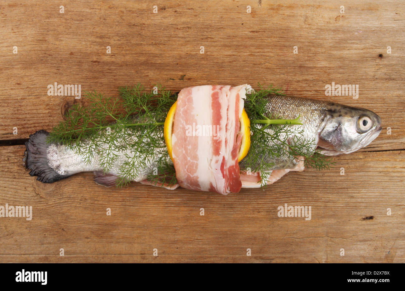 Ganze rohe Forelle gewickelt mit Pancetta, Zitrone und Fenchel auf einem rustikalen Holzbrett Stockfoto