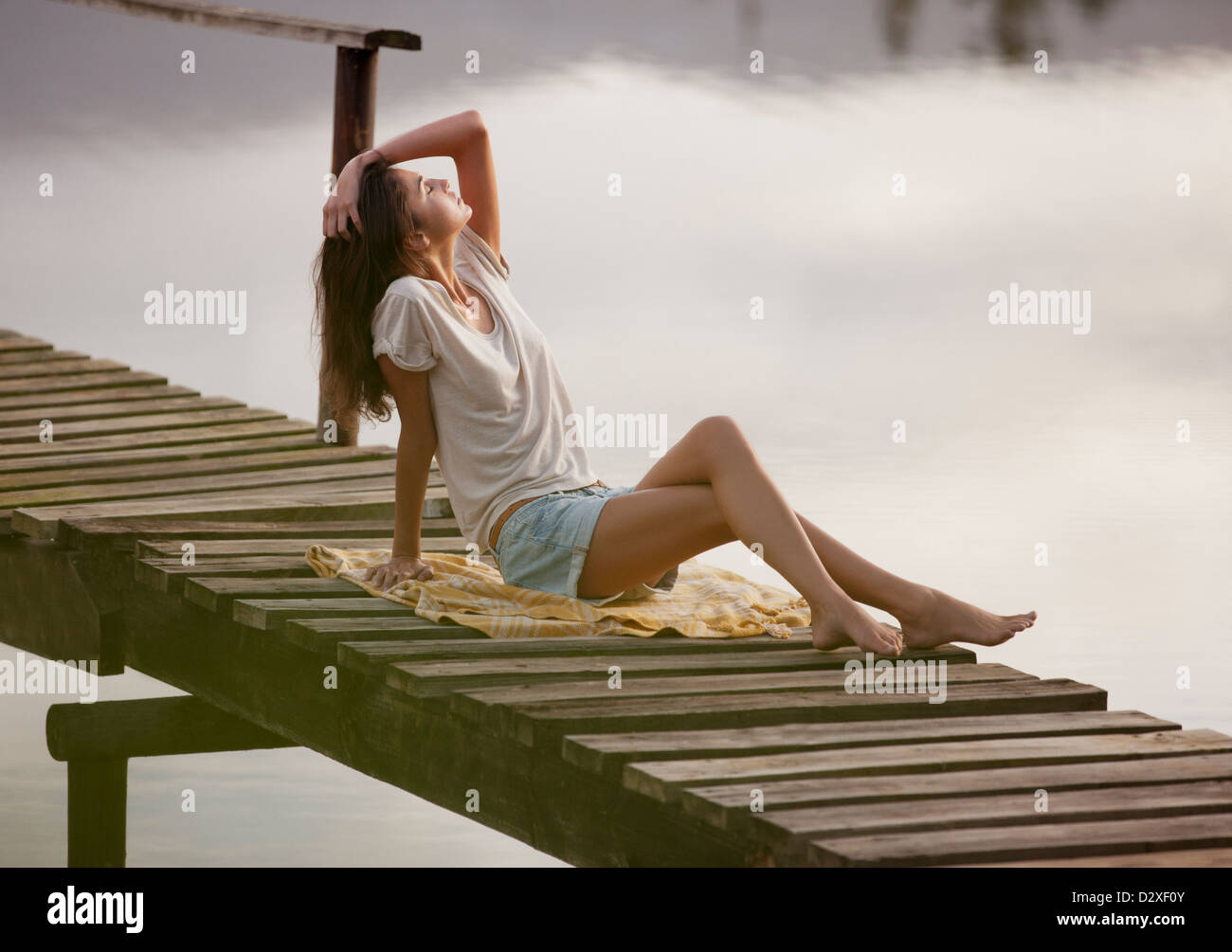 Frau mit Kopf in den Nacken und Hand im Haar auf Dock über See Stockfoto
