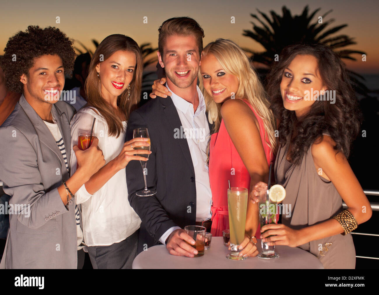 Porträt von lächelnden Freunde tranken Cocktails auf Balkon bei Sonnenuntergang Stockfoto