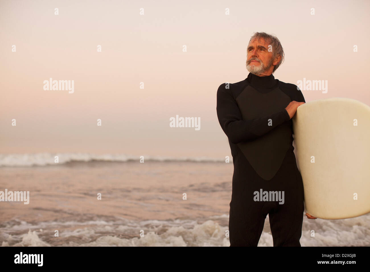 Ältere Surfer tragen Board am Strand Stockfoto