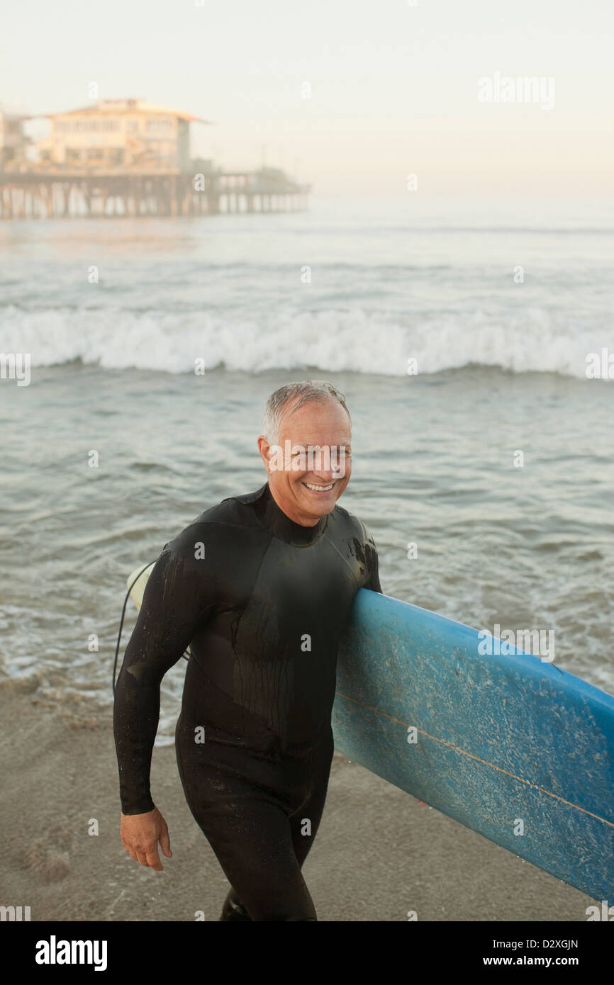 Ältere Surfer tragen Board am Strand Stockfoto