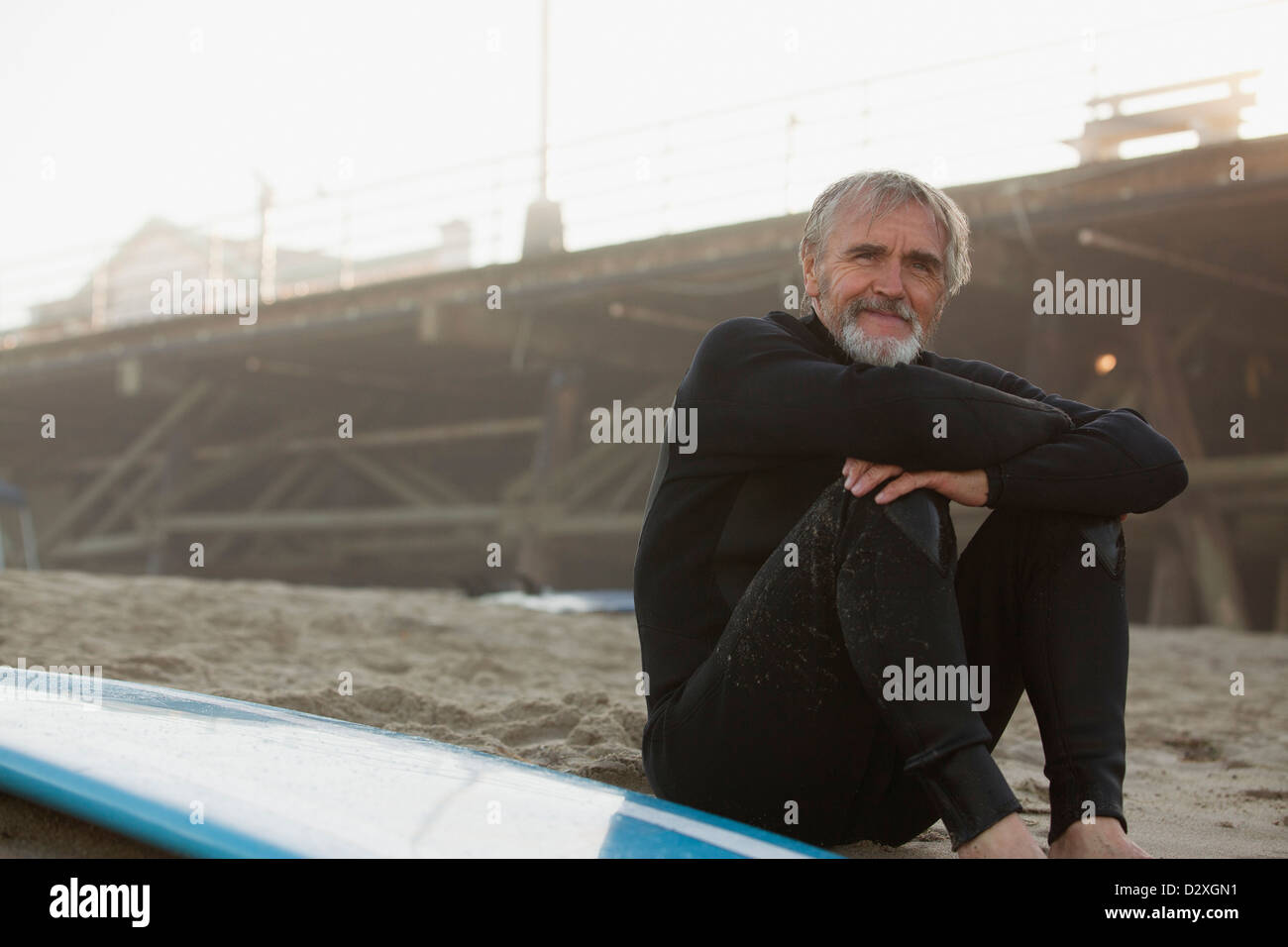 Ältere Surfer sitzen mit Board am Strand Stockfoto