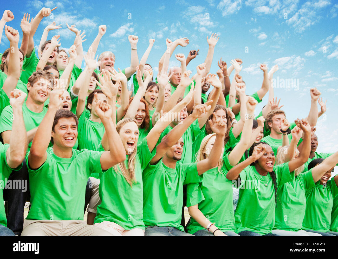 Drängen Sie sich in grünen T-shirts mit erhobenen Armen jubeln Stockfoto