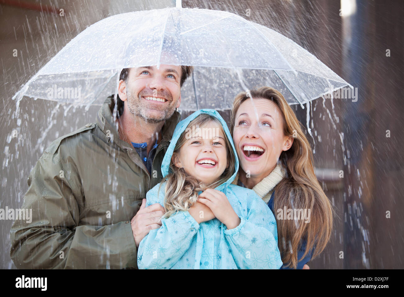 Begeisterte Familie unter Dach im Regen Stockfoto