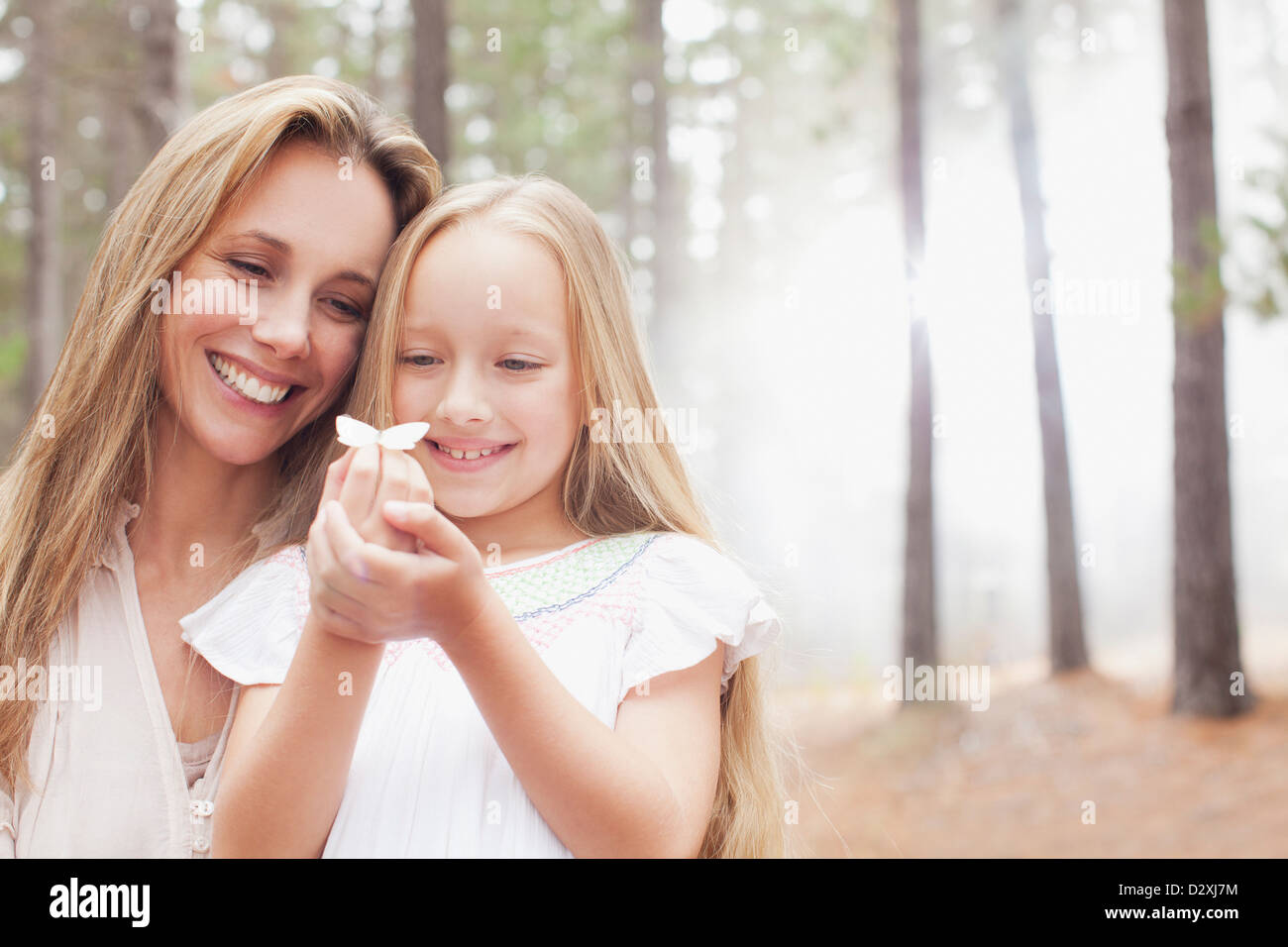 Lächelnde Mutter und Tochter halten Schmetterling im Wald Stockfoto