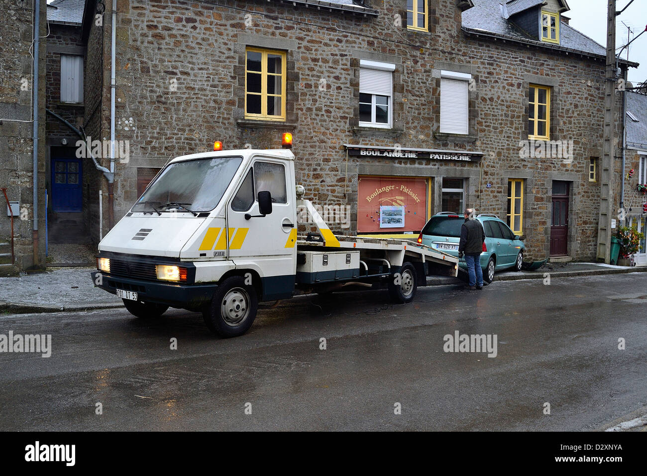 Ein Auto rutschte auf der vereisten Straße und endete seine laufen auf ein Haus, ein Abschleppwagen kommen, sie zurückzugewinnen. Stockfoto