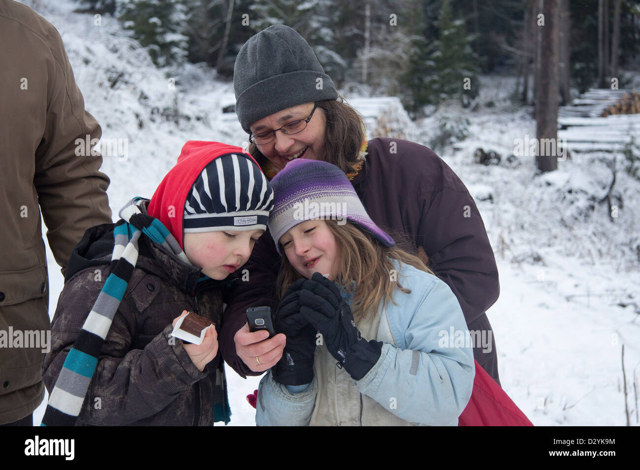 Mutter und Kinder betrachten von Fotos auf ihrem Handy Stockfoto