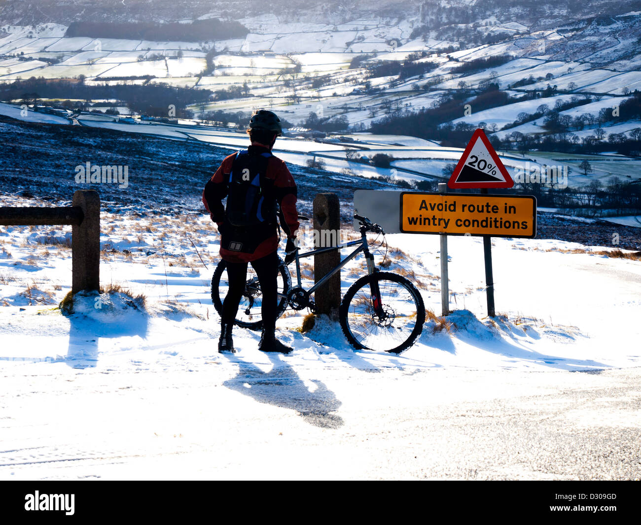 Ein Radfahrer ruht über eine vermeiden Route in winterlichen Bedingungen Zeichen auf einem steilen Hügel mit Blick auf Farndale im Schnee Stockfoto