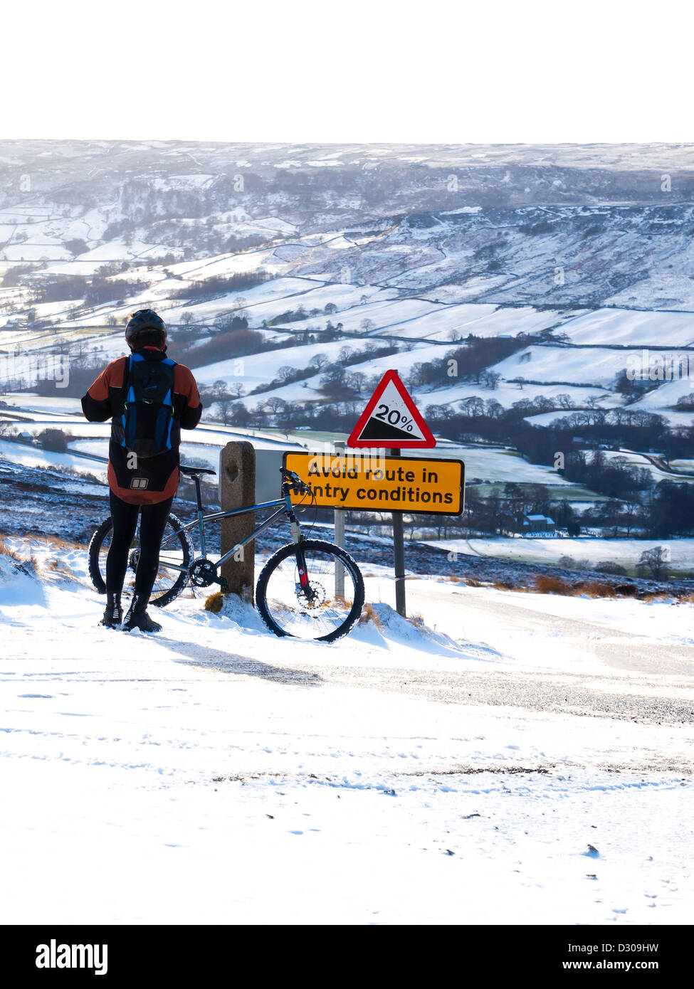 Ein Radfahrer ruht über eine vermeiden Route in winterlichen Bedingungen Zeichen auf einem steilen Hügel mit Blick auf Farndale im Schnee Stockfoto