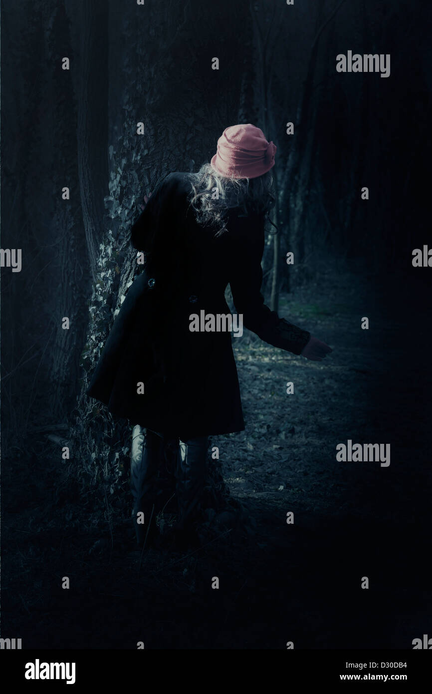 eine Frau mit einem schwarzen Mantel steht hinter einem Baum Stockfoto