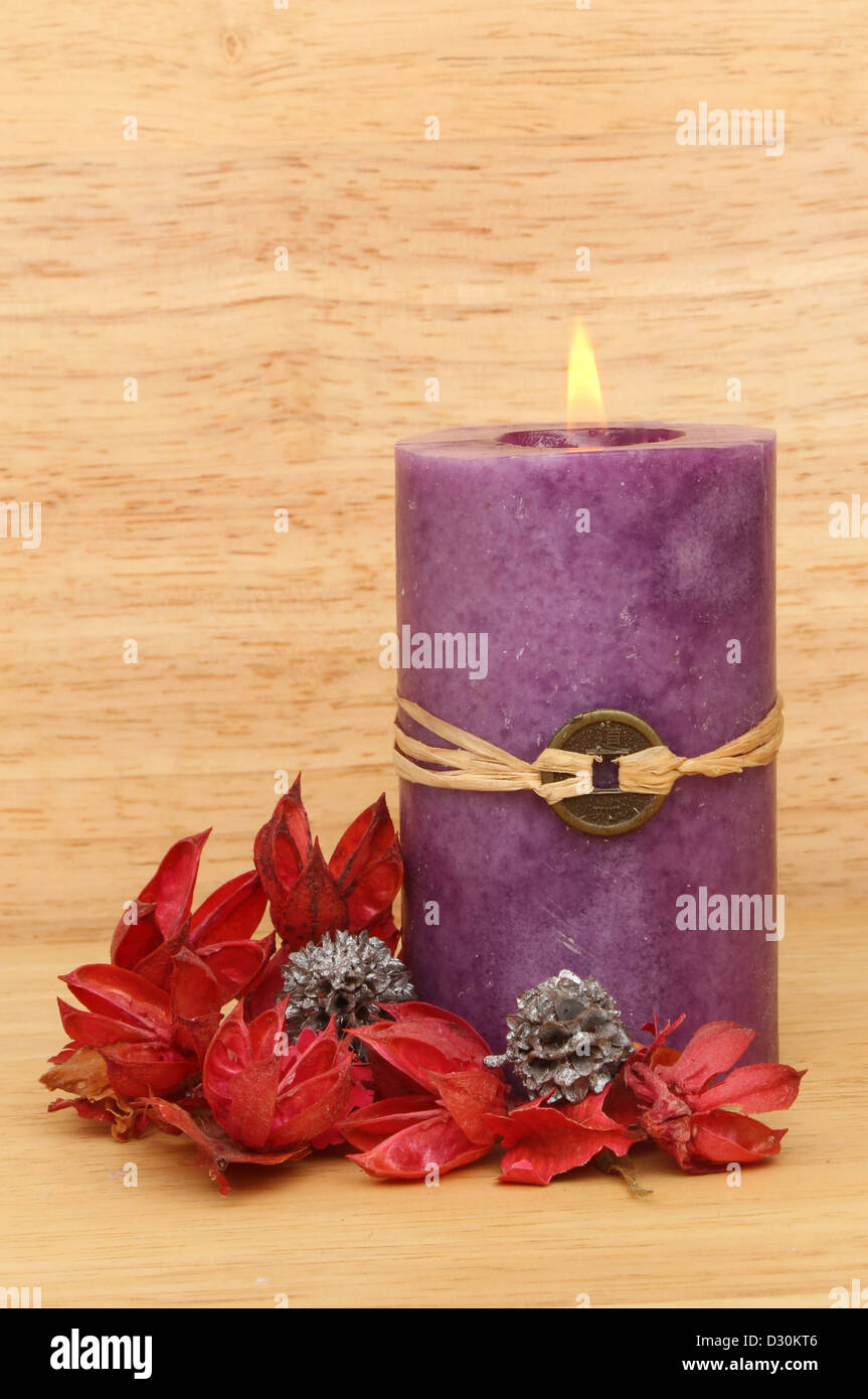Brennende Kerze Feng Shui und Potpourri gegen eine Bachground warmes farbiges Holz lila Stockfoto