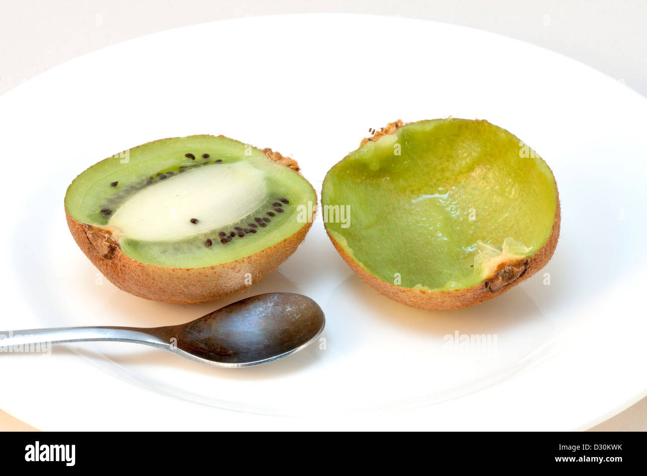 Kiwis in Scheiben geschnitten in Hälften auf einem weißen Teller, eines der Hälfte gegessen Stockfoto