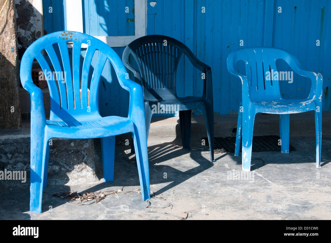 Drei blaue Plastikstühle durch eine blaue Tür. Stockfoto