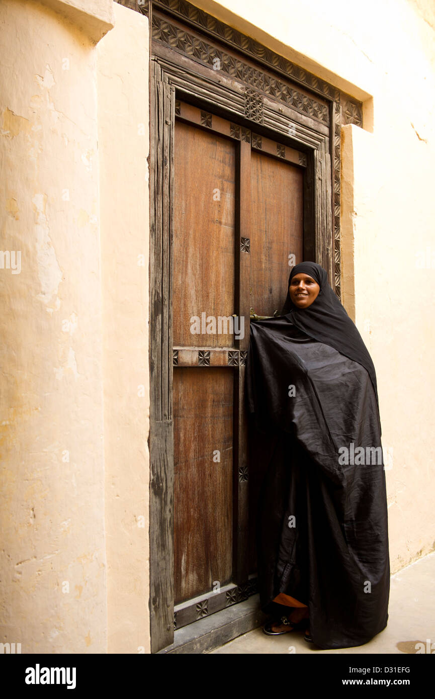 Swahili-Frau steht an einer traditionellen Zanzibar-Tür in der alten Festung, Lamu, Lamu Archipel, Kenia Stockfoto