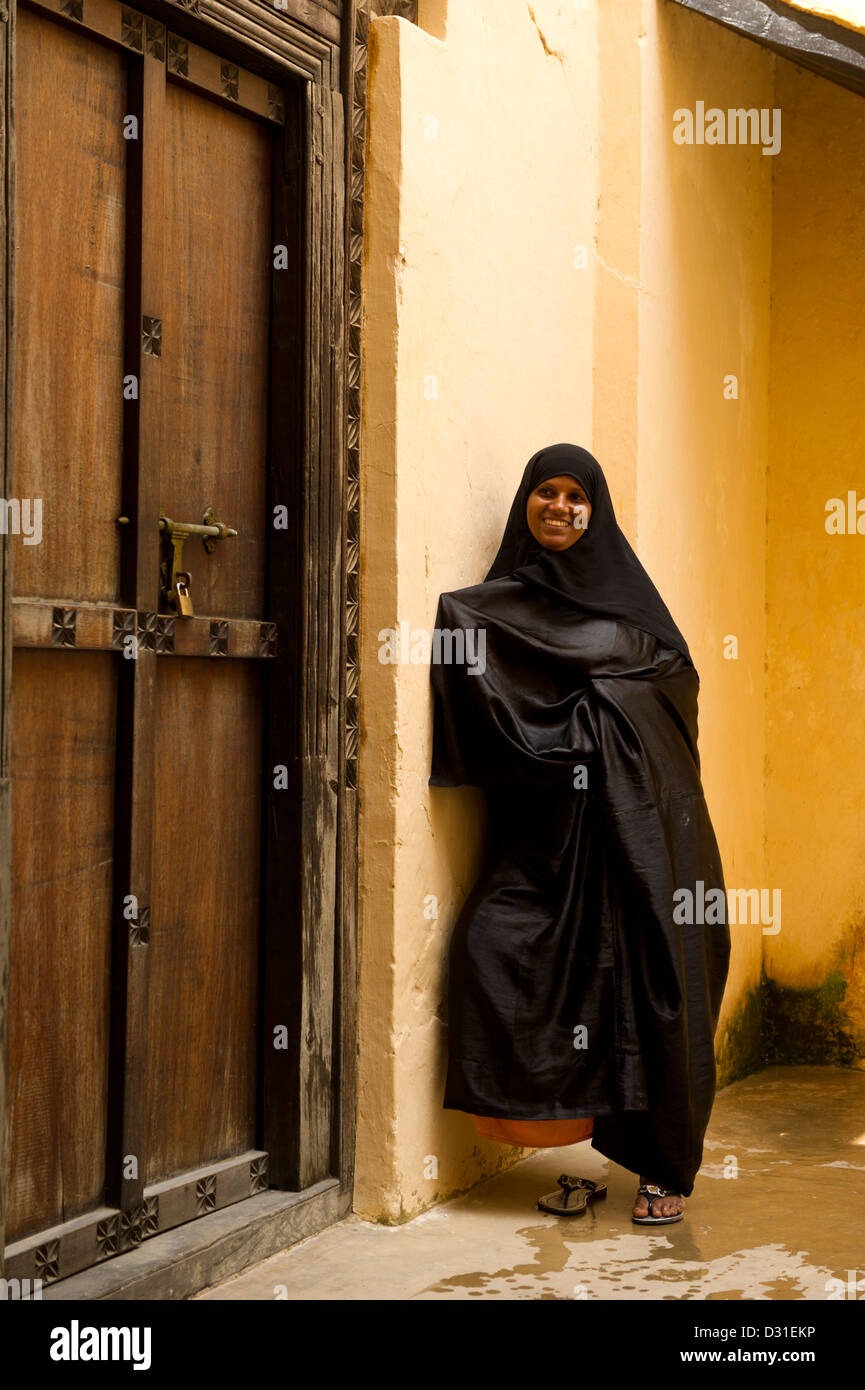 Swahili-Frau steht an einer traditionellen Zanzibar-Tür in der alten Festung, Lamu, Lamu Archipel, Kenia Stockfoto