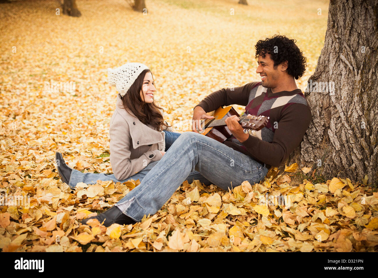 Mann spielt Gitarre für Freundin im Herbstlaub Stockfoto