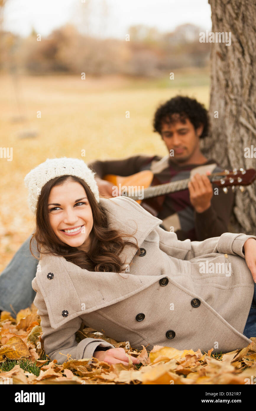 Mann spielt Gitarre für Freundin im Herbstlaub Stockfoto