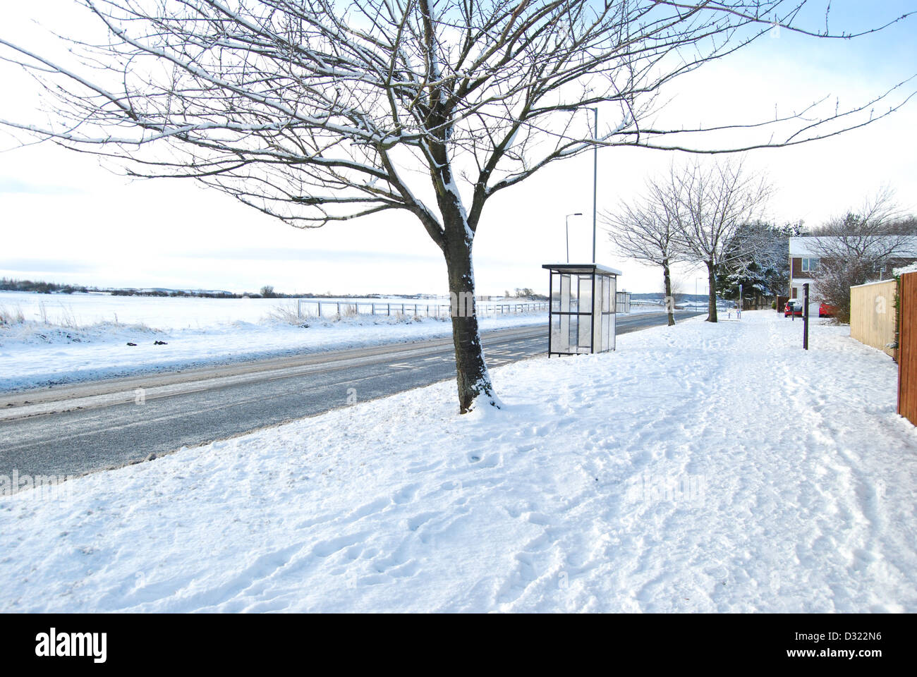 A Dick Schnee bedeckten Straße und kein Splitt auf der Straße mit Bushaltestelle und Baum und strahlend blauen Himmel in einer ländlichen Wohngegend Stockfoto