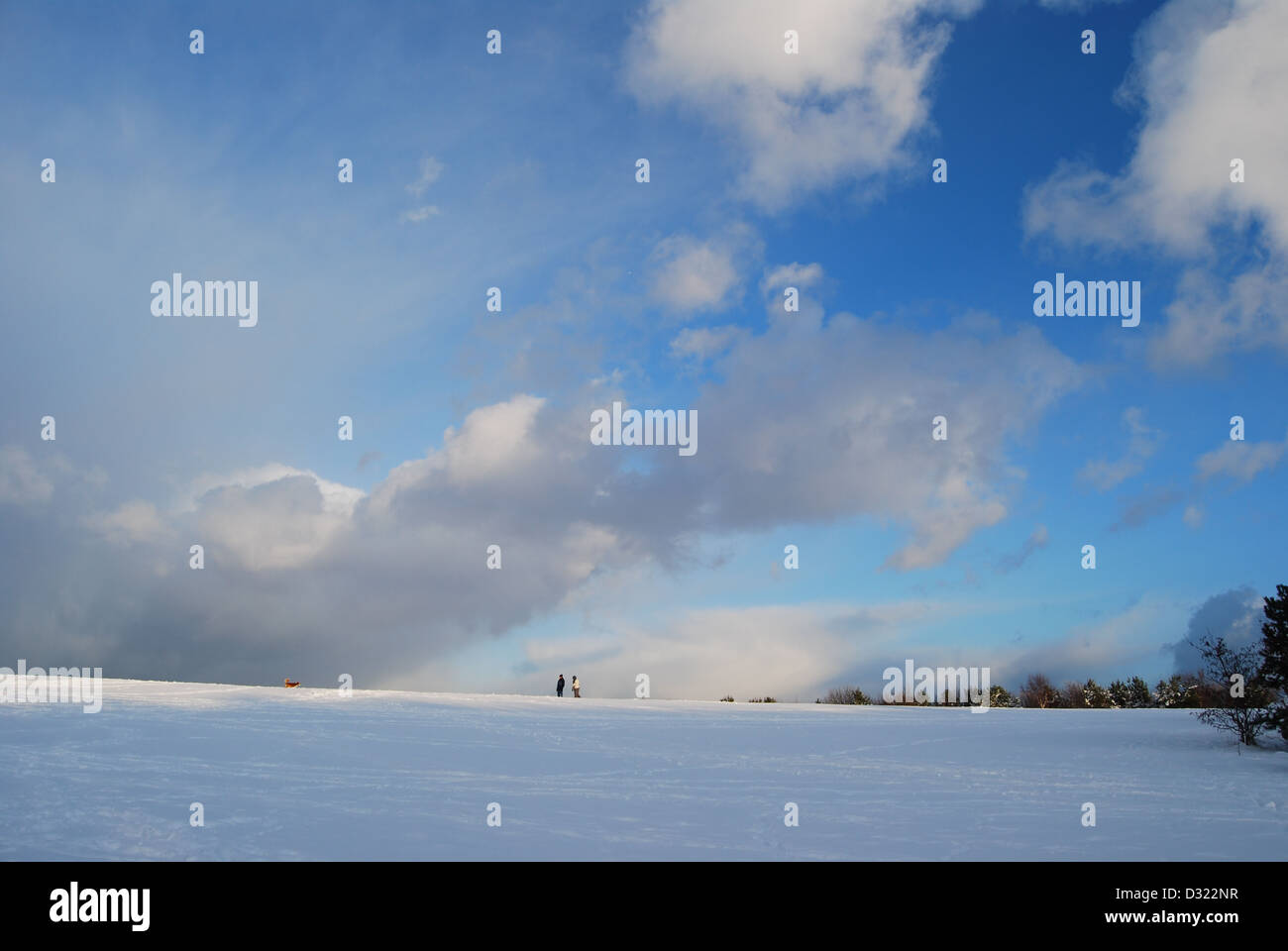 Einen dramatischen Verlauf der dunklen und hellen blauen Himmel und Wolken mit Blick auf eine große Decke von Schnee auf einem Feld mit Menschen am Horizont Stockfoto
