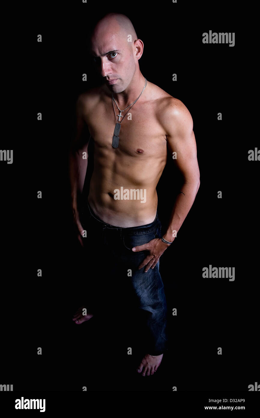 Eine schlanke junge Mann stehend suchen seriöse und starrte direkt in der Kamera mit den Händen in seine Jeans Jean Taschen und kein Hemd Stockfoto