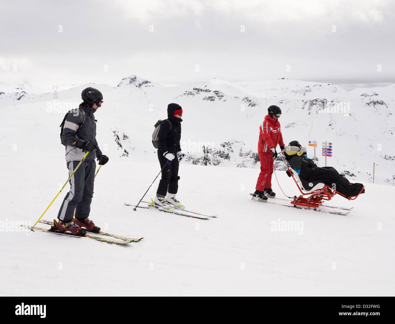 Skifahrer helfen behinderten Sitskier in einem Tessier Tandem'Flex Sitski Skifahren in Grand Massif Skigebiet der französischen Alpen. Frankreich Stockfoto