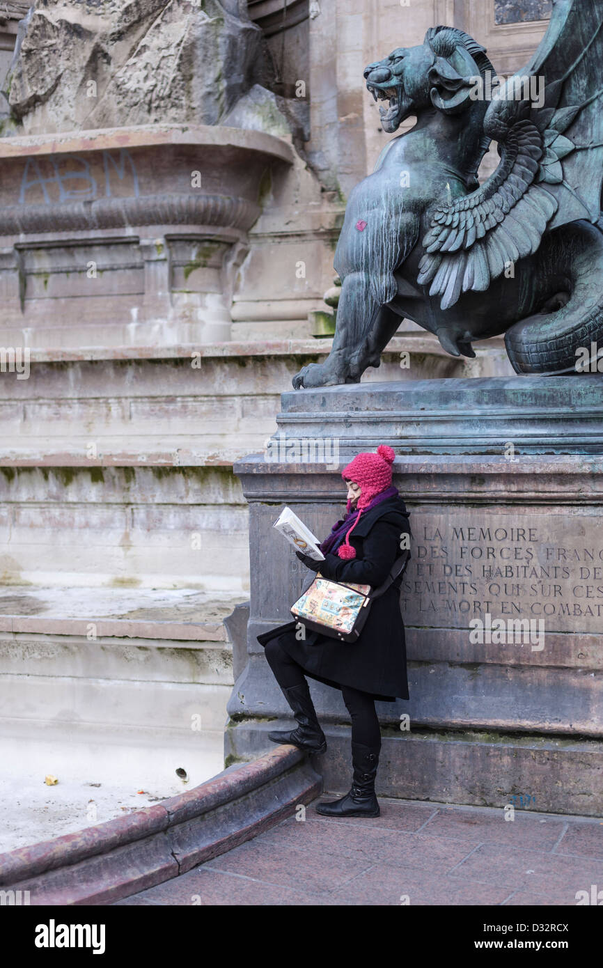 Ein Mädchen lesen bei kaltem Wetter unter einem Drachen (von Henri Alfred Jacquemart) der Fontaine Saint-Michel, Paris, Frankreich Stockfoto