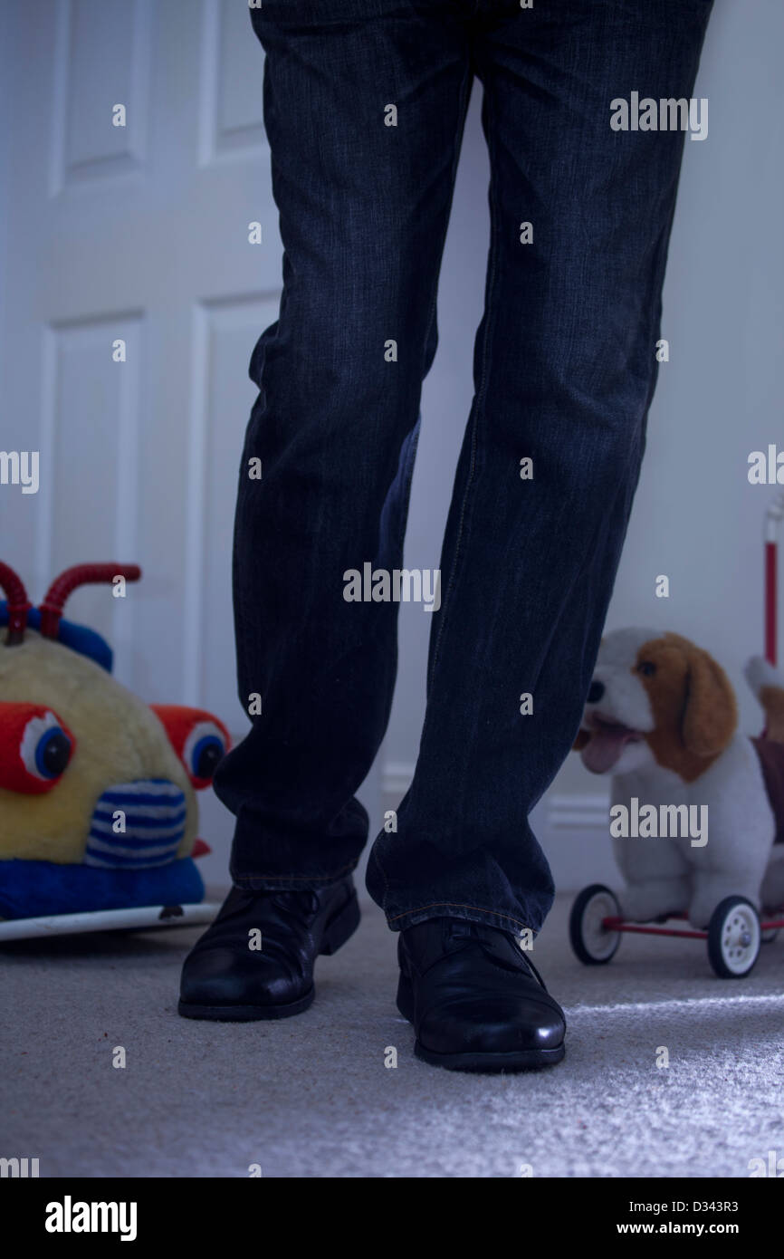 Männliche Beine zu Fuß in ein düster beleuchteten Kinderzimmer mit Tür, Spielzeugauto und Spielzeughund im Hintergrund. Stockfoto