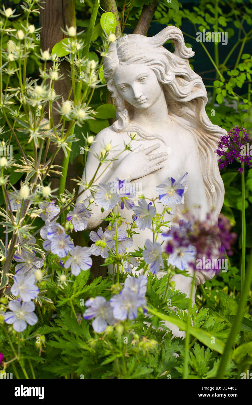 Statue der Frau im Bett mit Geranium Plitsch Splash, Eryngium, Allium. Stockfoto