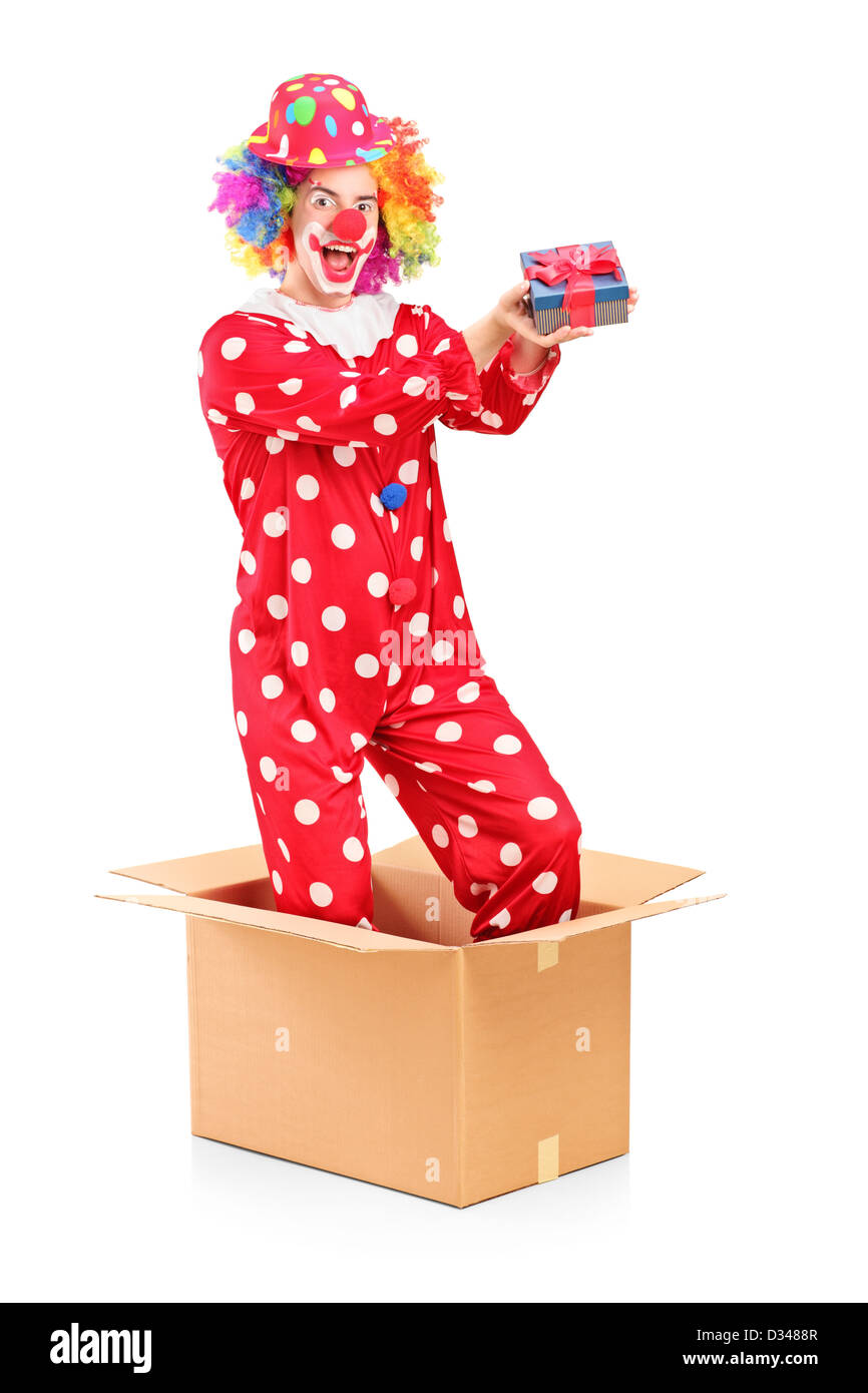 Ein Lächeln auf den Lippen Clown in einem Karton hält ein Geschenk isoliert auf weißem Hintergrund Stockfoto