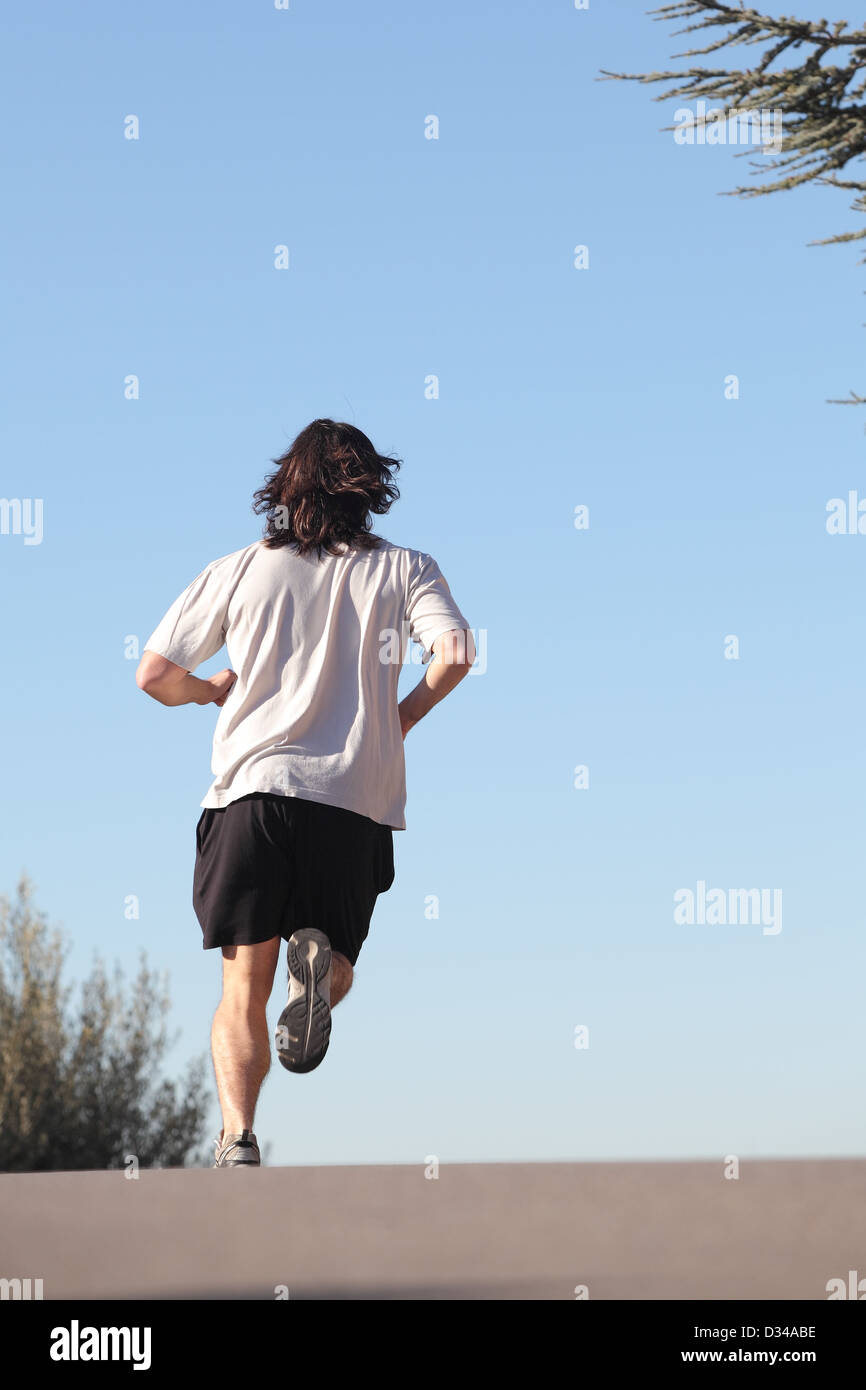 Rückansicht eines Mannes auf eine Straße mit dem Himmel im Hintergrund laufen Stockfoto