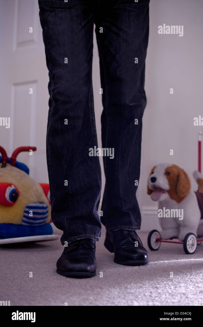 Ein Mann, nur zu Fuß in ein Kinderzimmer mit Spielzeug neben ihm Beine. Stockfoto