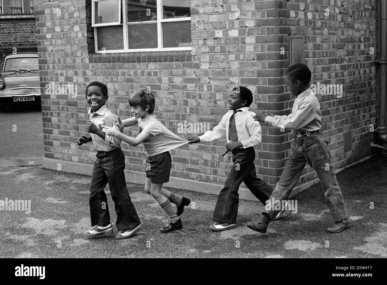 Grundschule Spielplatz. Jungs spielen zusammen. South London. 70er Jahre multirassische multi ethnischen schwarz und weiß Kinder mit Spaß Spielzeit in der Schule 70er Jahre UK HOMER SYKES Stockfoto