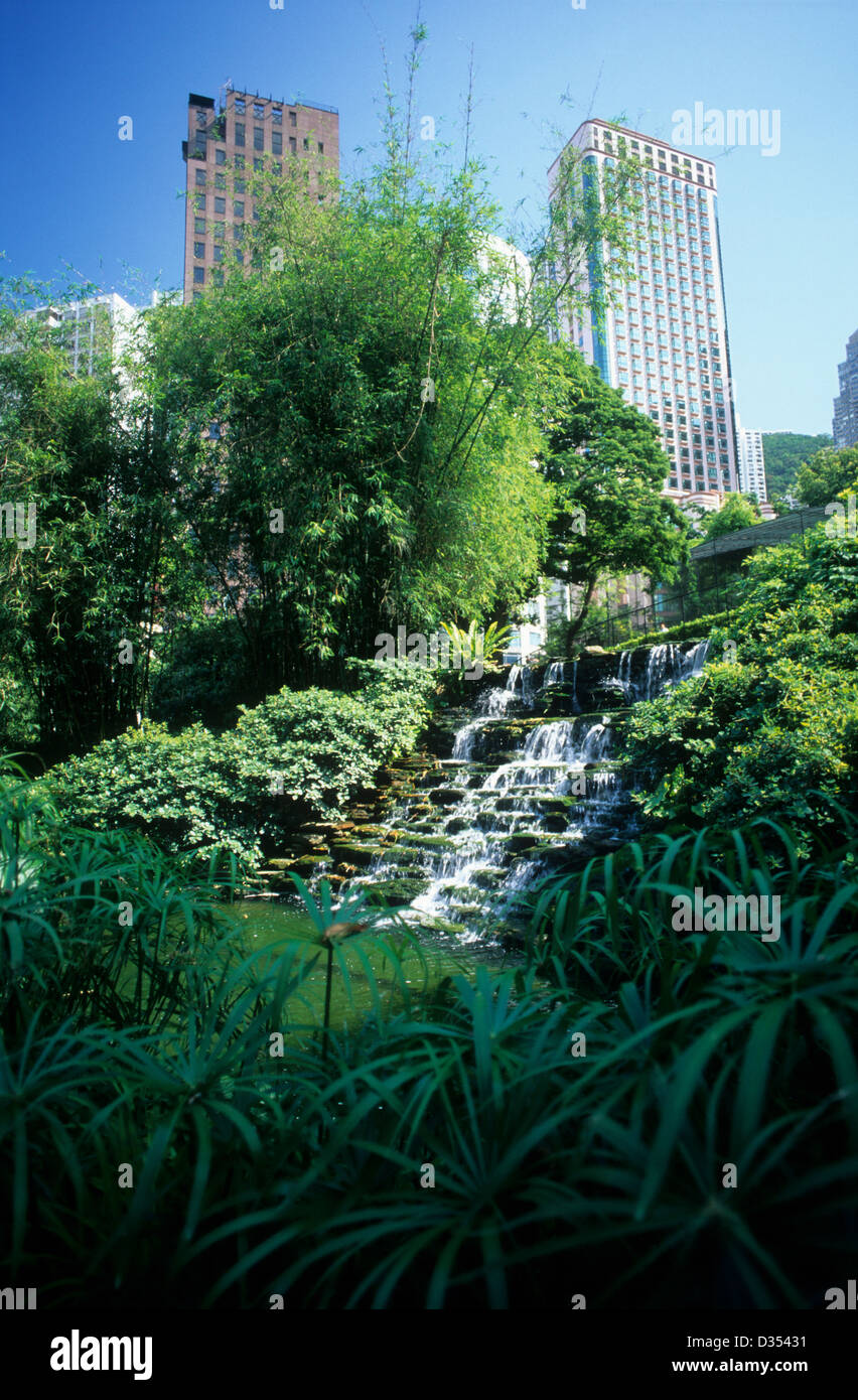 China, Hong Kong, Hong Kong Island, Wasserfall im Botanischen Garten mit Hochhäusern im Hintergrund. Stockfoto