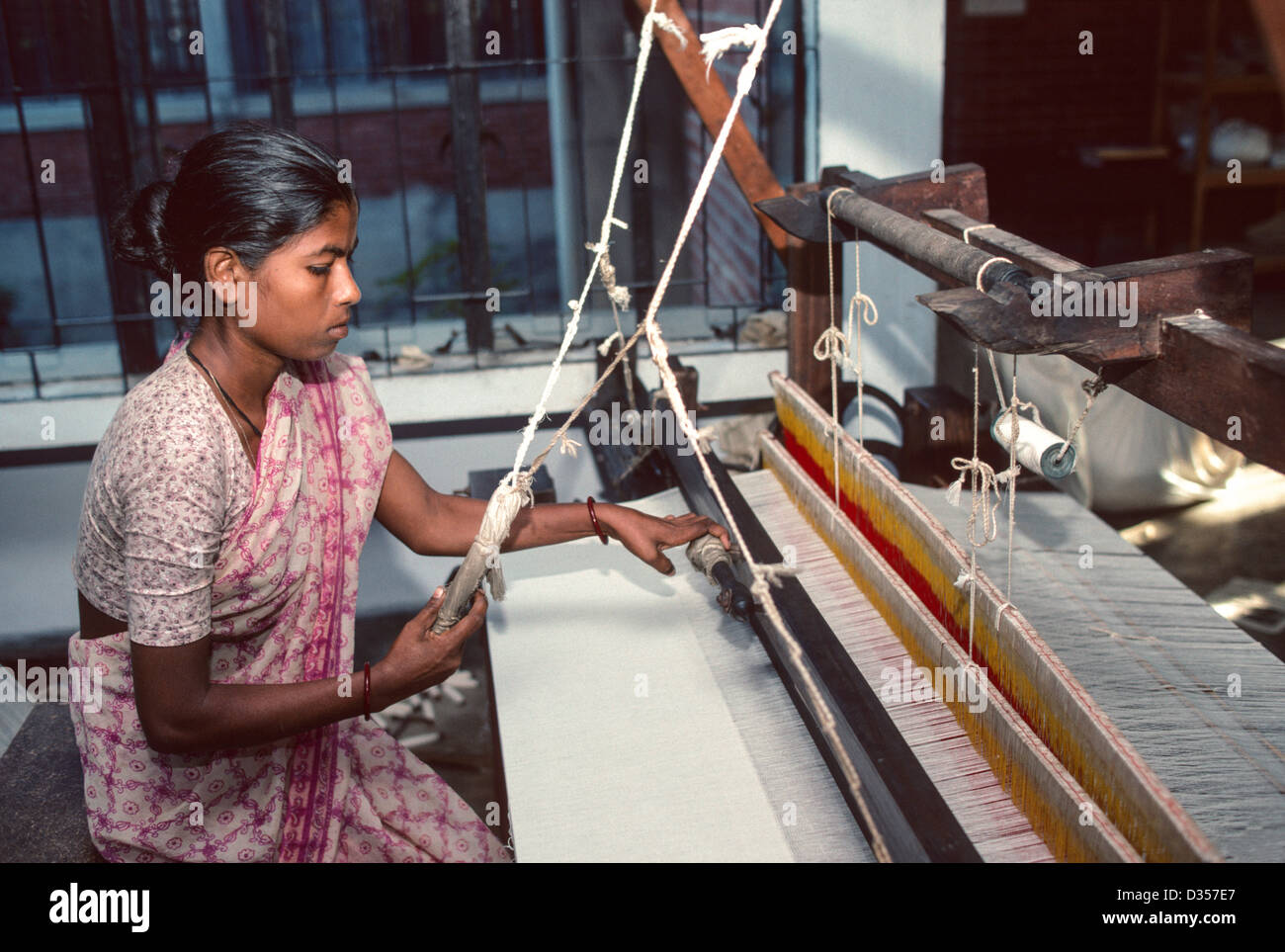 Junge Frau webt Tuch auf einem traditionellen hölzernen Handwebstuhl. Manikganj, Bangladesch Stockfoto