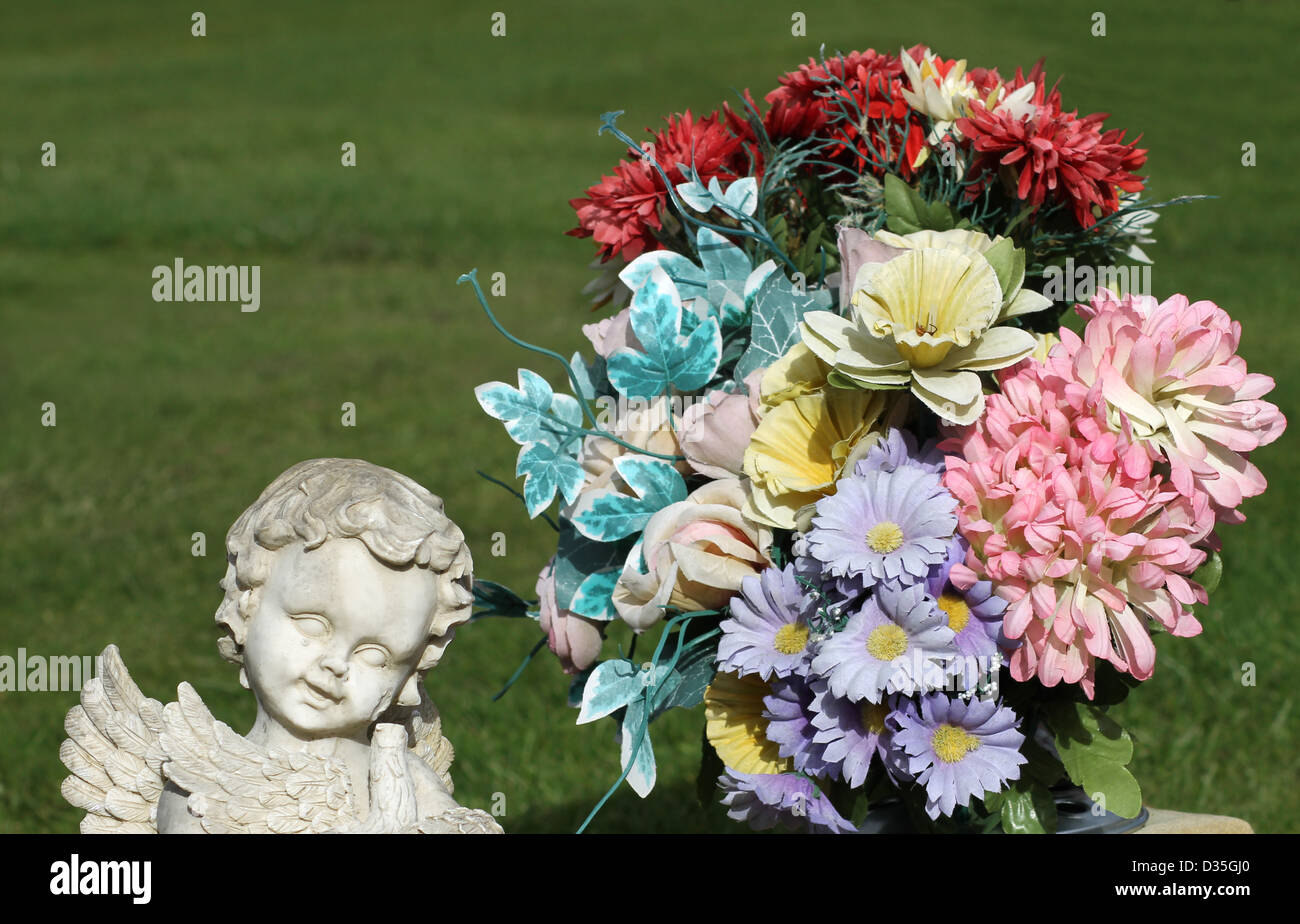 Winkel-Statue im Friedhof neben Blumenstrauß. Rasen Sie im Hintergrund mit Textfreiraum. Stockfoto
